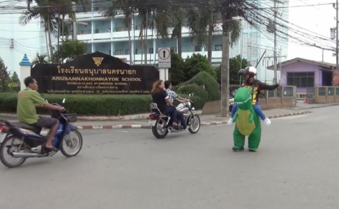 ตำรวจสวมชุดมาสคอตไดโนเสาร์ยืนโบกรถ